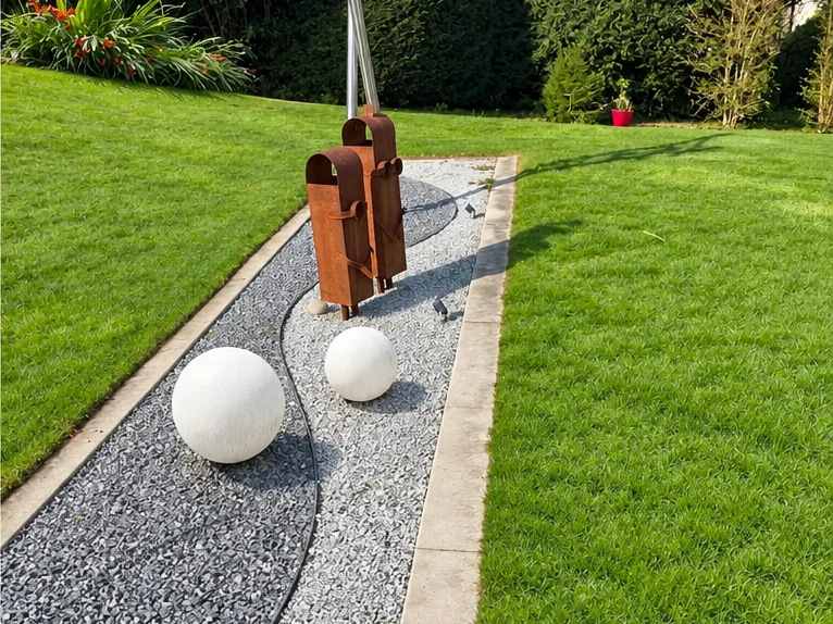 Nachher: dichter, grüner Rasen entlang eines Kieswegs mit Gartenskulptur
